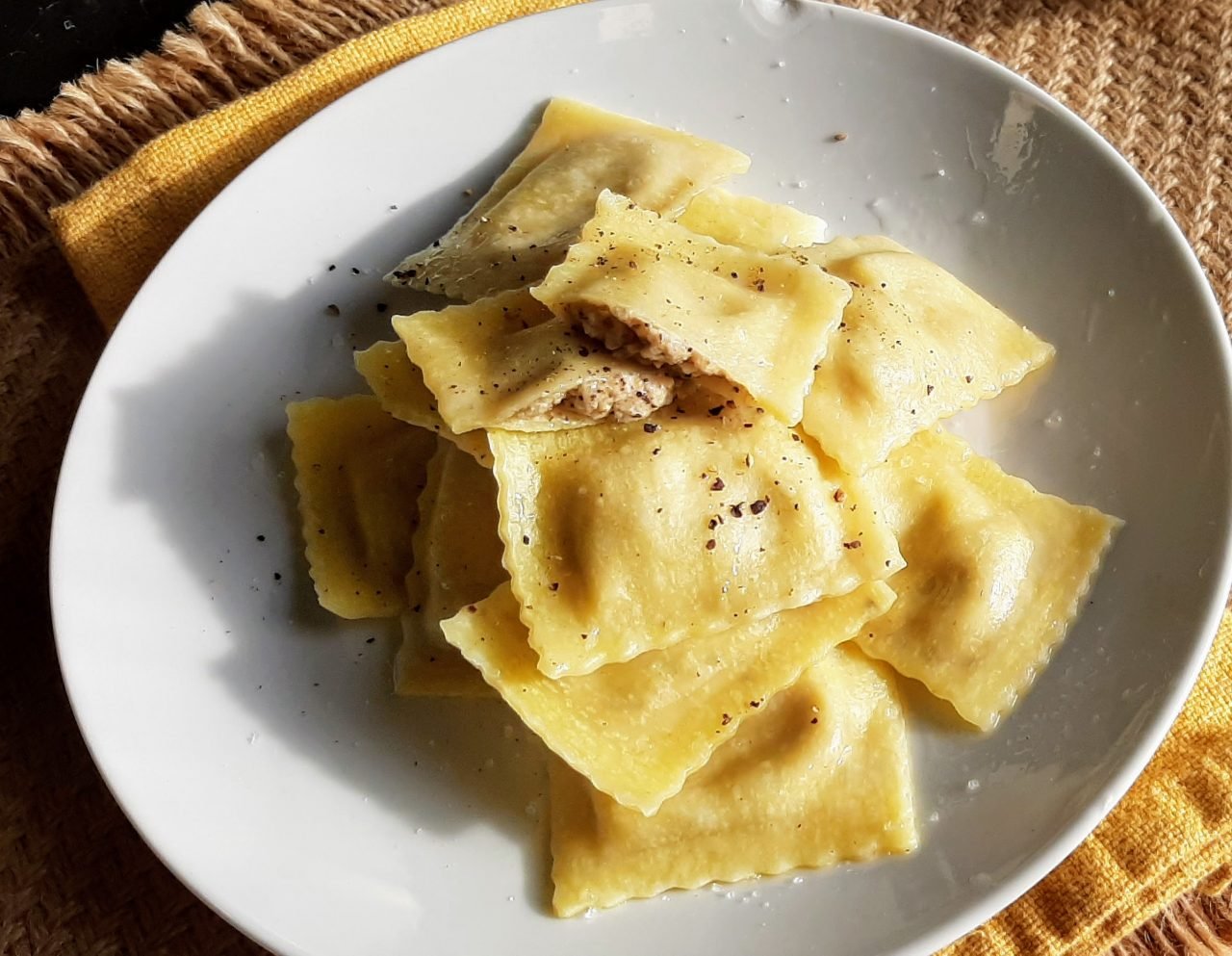 Fresh ravioli on a white plate with cracked pepper
